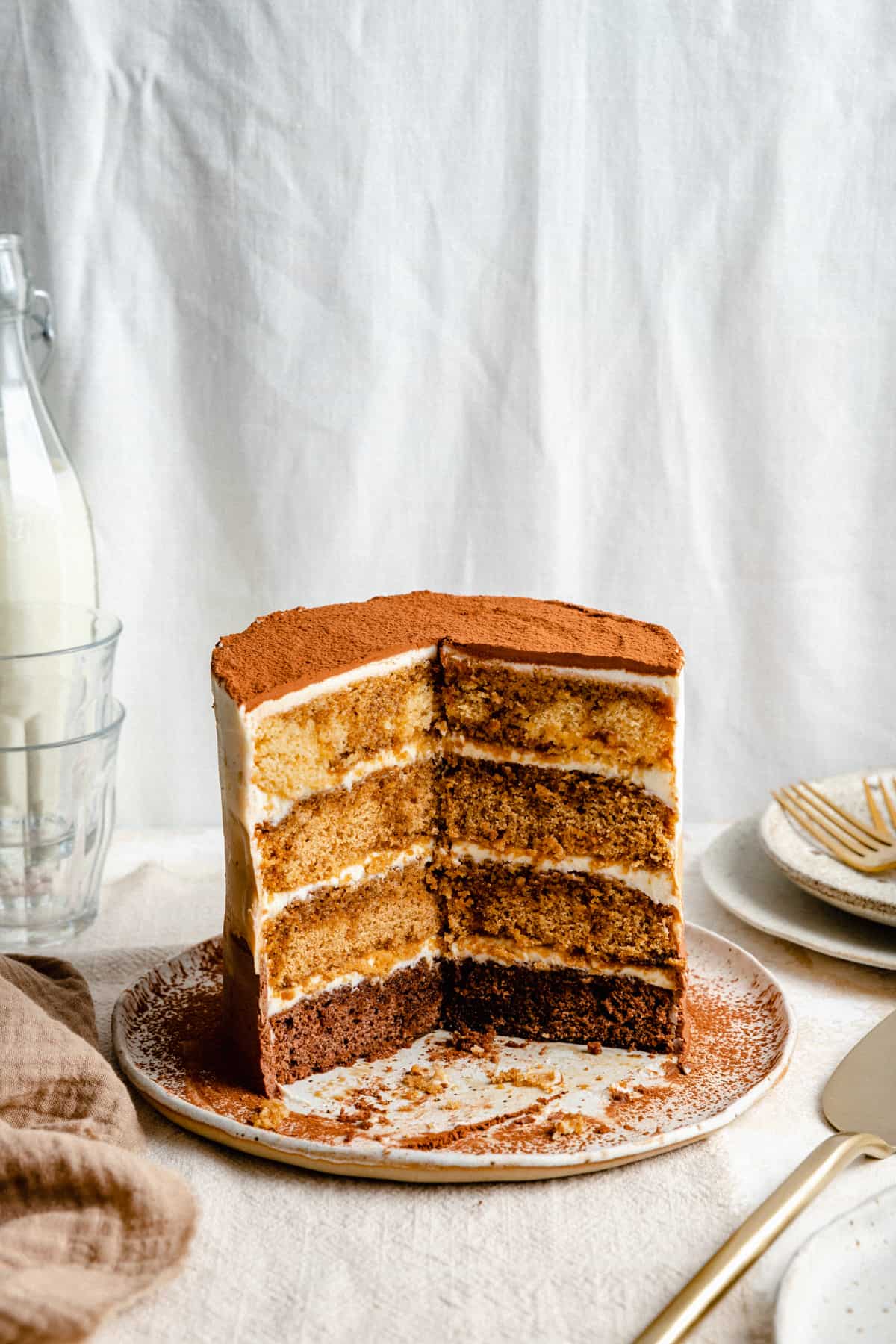 Tiramisu cake on a plate with a large wedge taken out showing the layers and insides. 