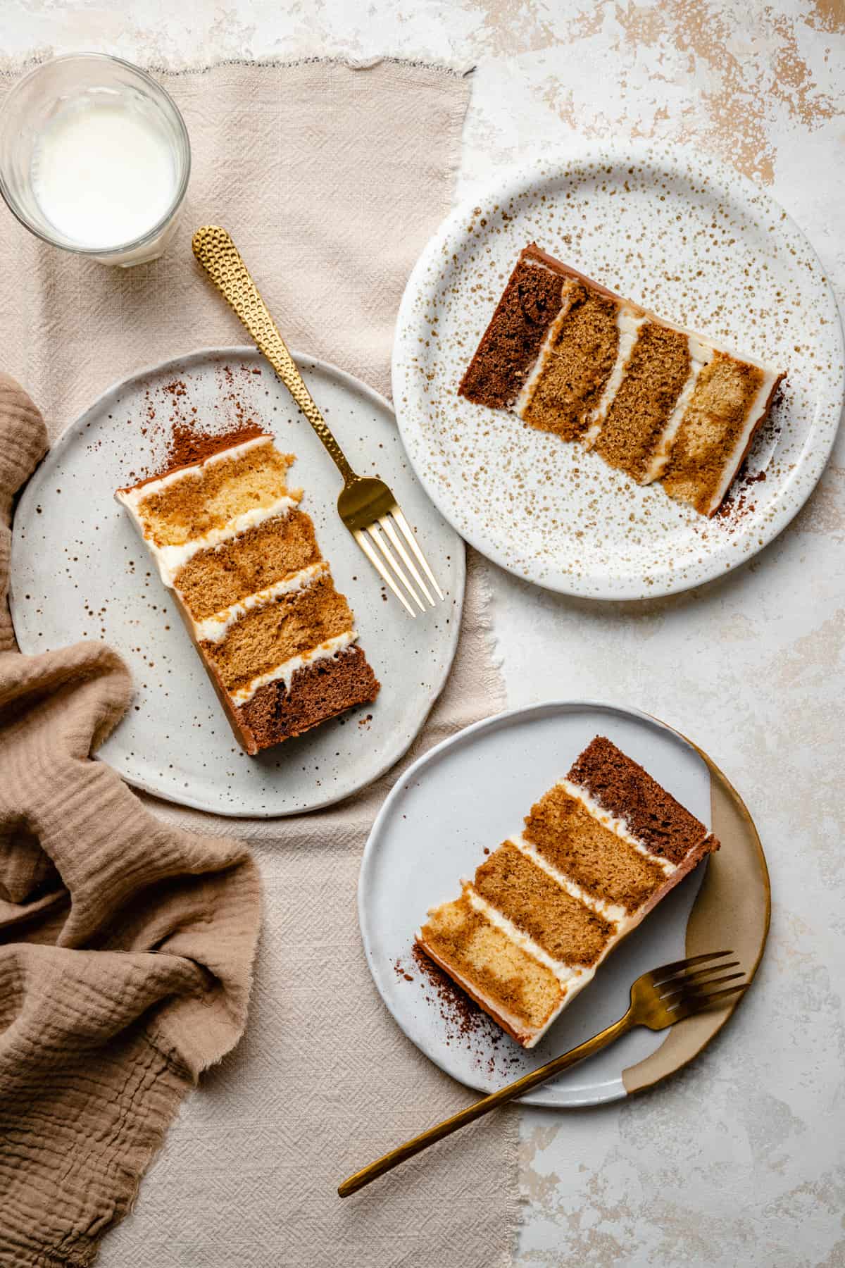 Three plates with slices of tiramisu cake with golden forks and a glass of milk. 