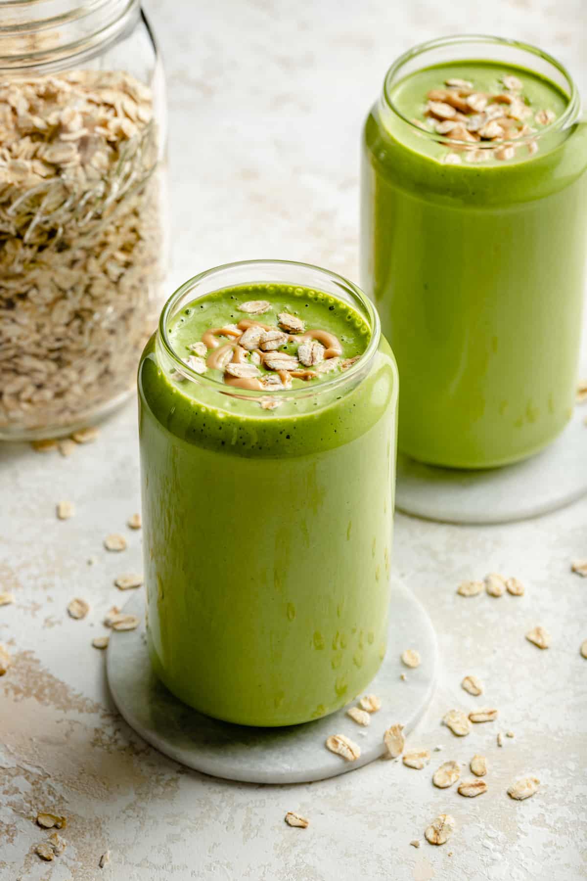 Two glasses of banana spinach smoothie with oats and cashew butter on.