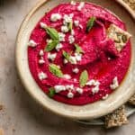 beetroot hummus in a bowl with crackers around on a plate.