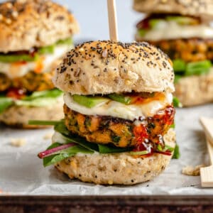 Salmon slider on parchment lined baking sheet with lime mayo and chilli jam and a skewer.