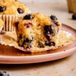 Blueberry sourdough muffins on a plate, one open and with a bite taken out of showing the insides.