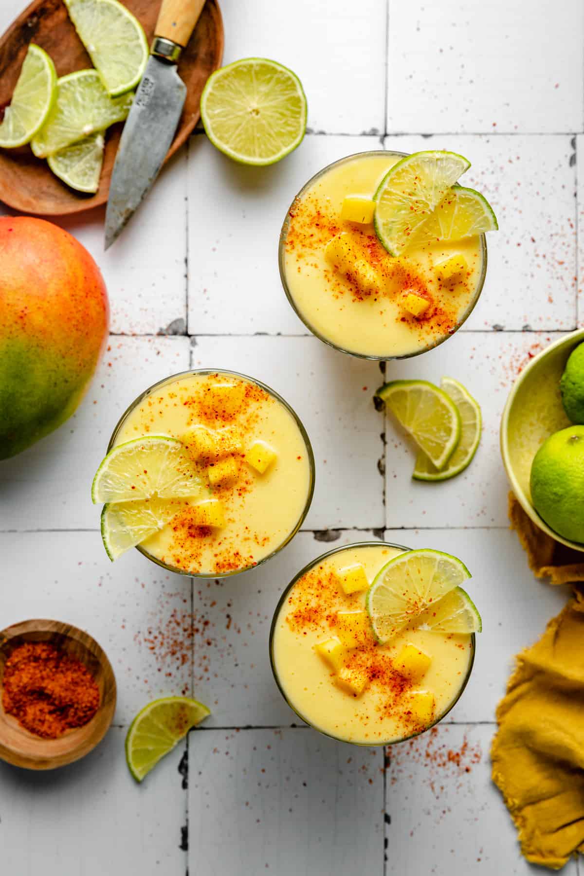 Three glasses of mango pineapple smoothie topped with mango lime and tajin.