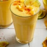 Glasses of mango pineapple smoothie on a tiled surface with tajin, mango and lime on top.