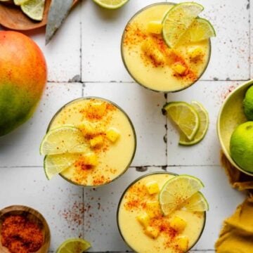Three glasses of mango pineapple smoothie topped with mango lime and tajin.