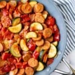 Chicken sausage and vegetables in a skillet with a stripy napkin.