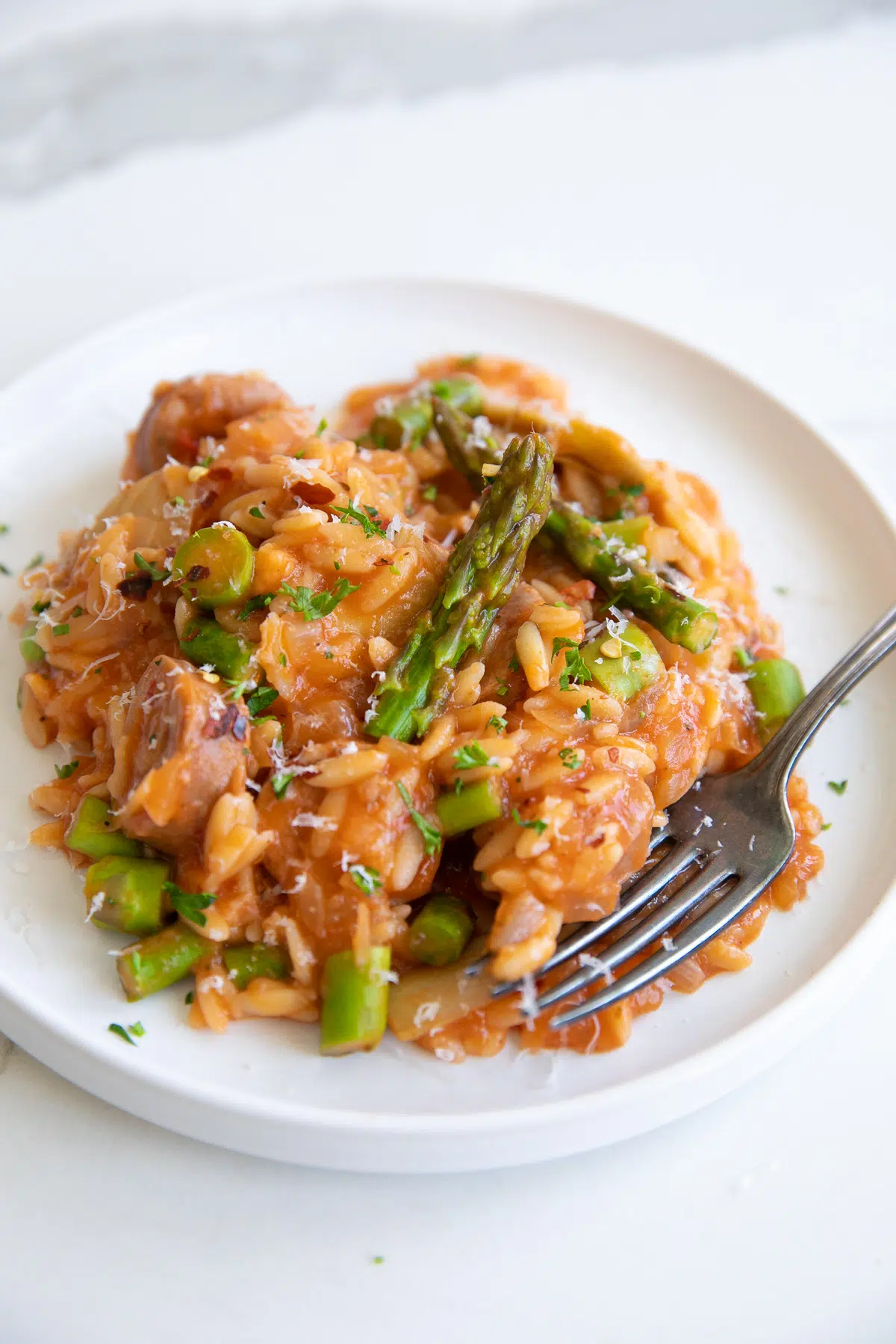 tomato orzo pasta with chicken sausage served on a plate with a fork.