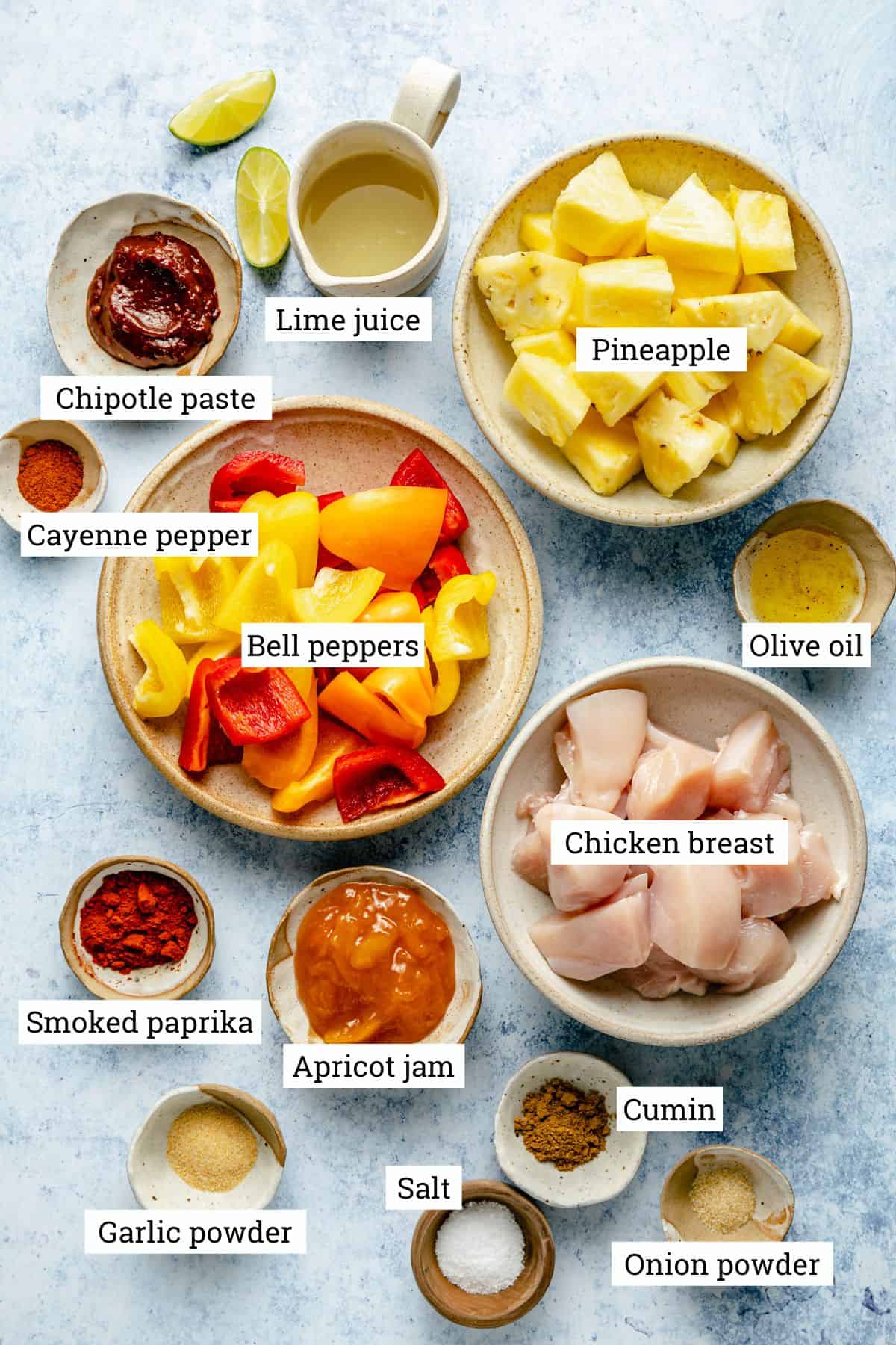 Ingredients for pineapple chicken kabobs in various bowls with labels.