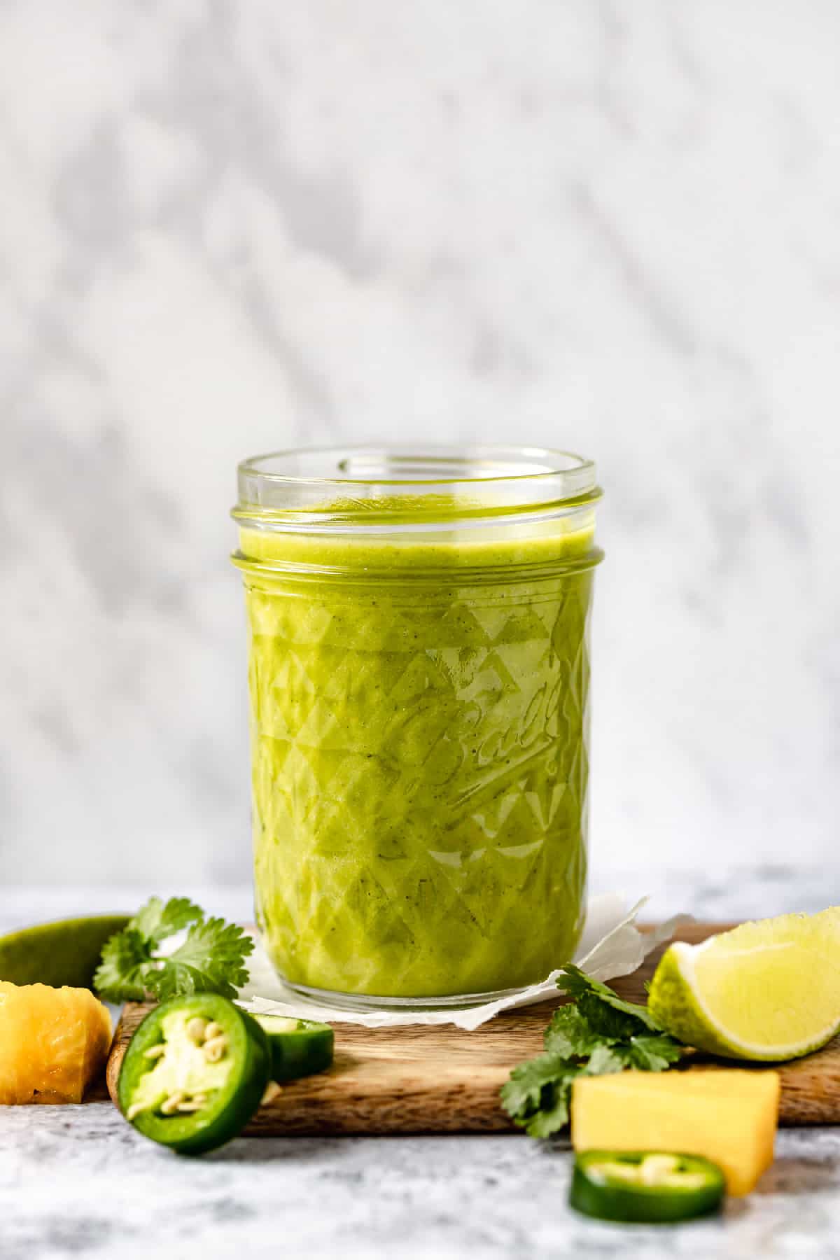 Pineapple chicken marinade in a jar with cilantro, lime and jalapeno around.