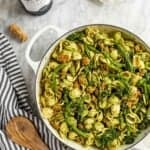 Chicken sausage pesto pasta in a skillet with spoon, wine and parmesan.