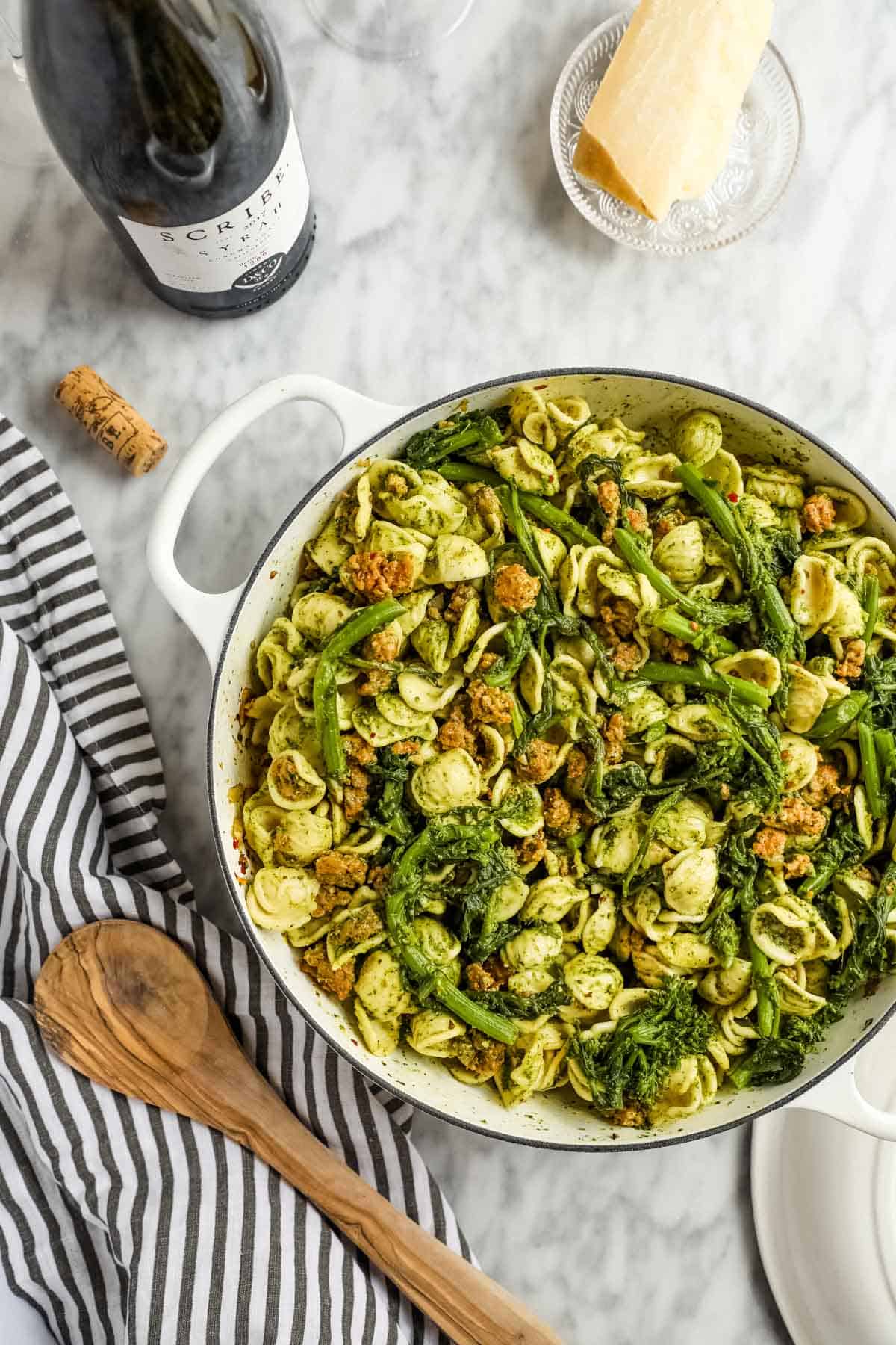 Chicken sausage pesto pasta in a skillet with spoon, wine and parmesan.