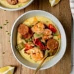 Shrimp and grits with chicken sausage in two bowls on a board.