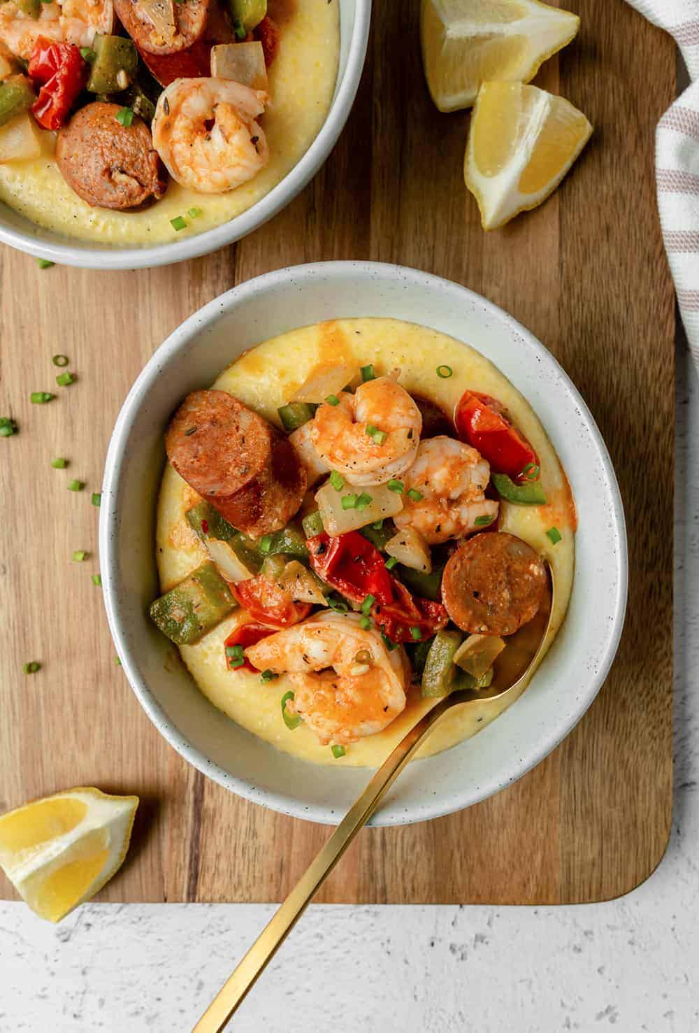Shrimp and grits with chicken sausage in two bowls on a board. 