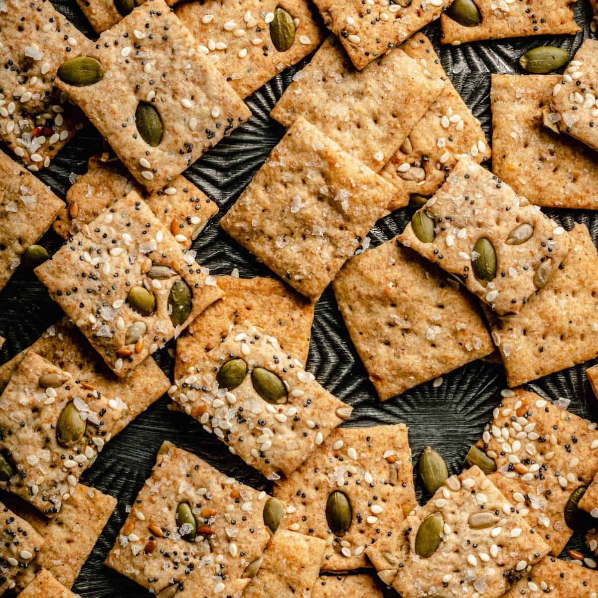 An array of sourdough crackers on a baking sheet showing the crisp texture and seeds on top. 
