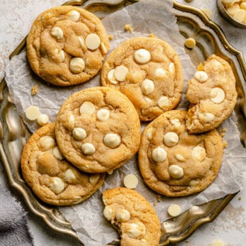 lemon white chocolate cookies on a golden platter lined with parchment paper with one broken in half.