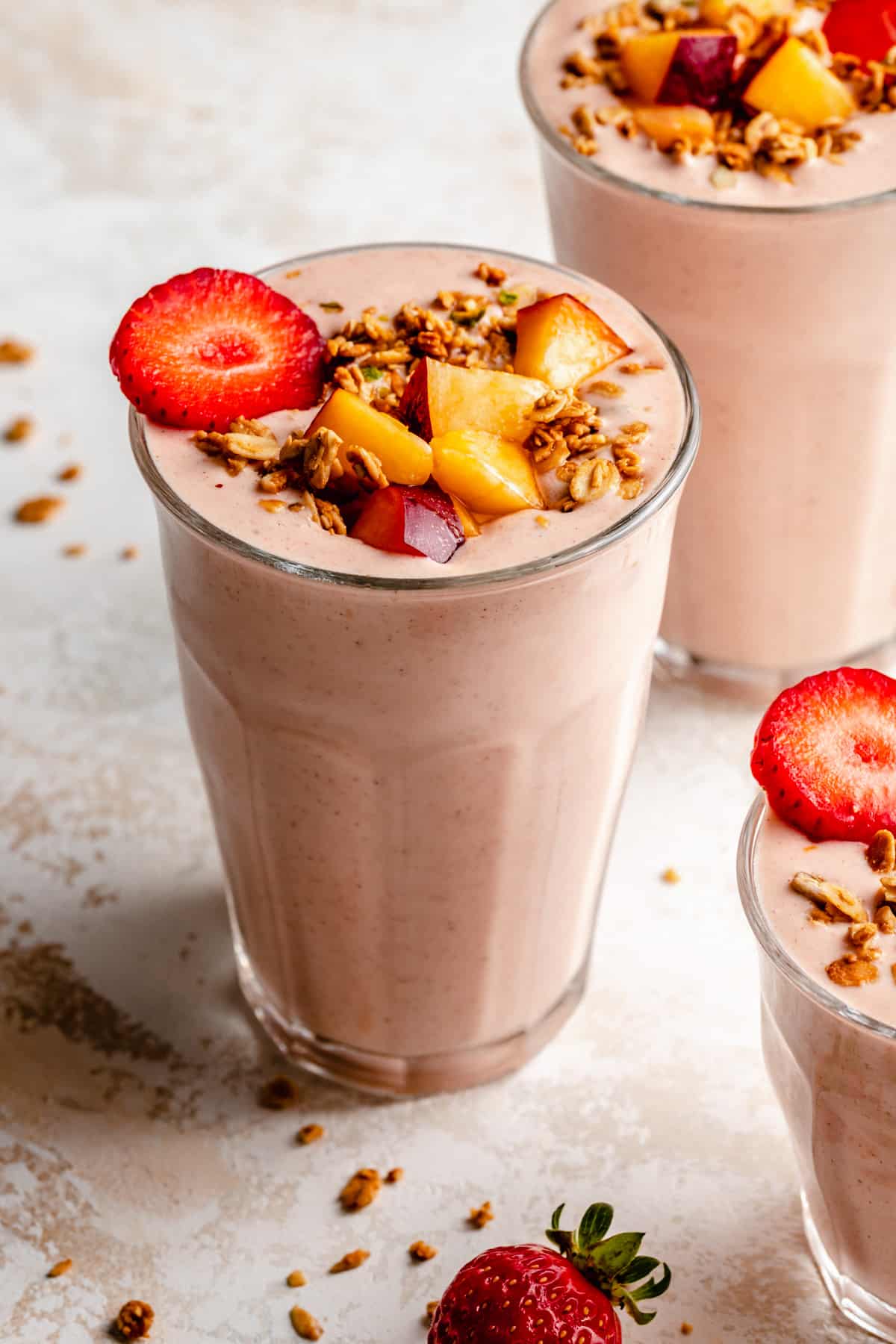 Glasses of strawberry peach smoothie with chopped fruit and granola on top.