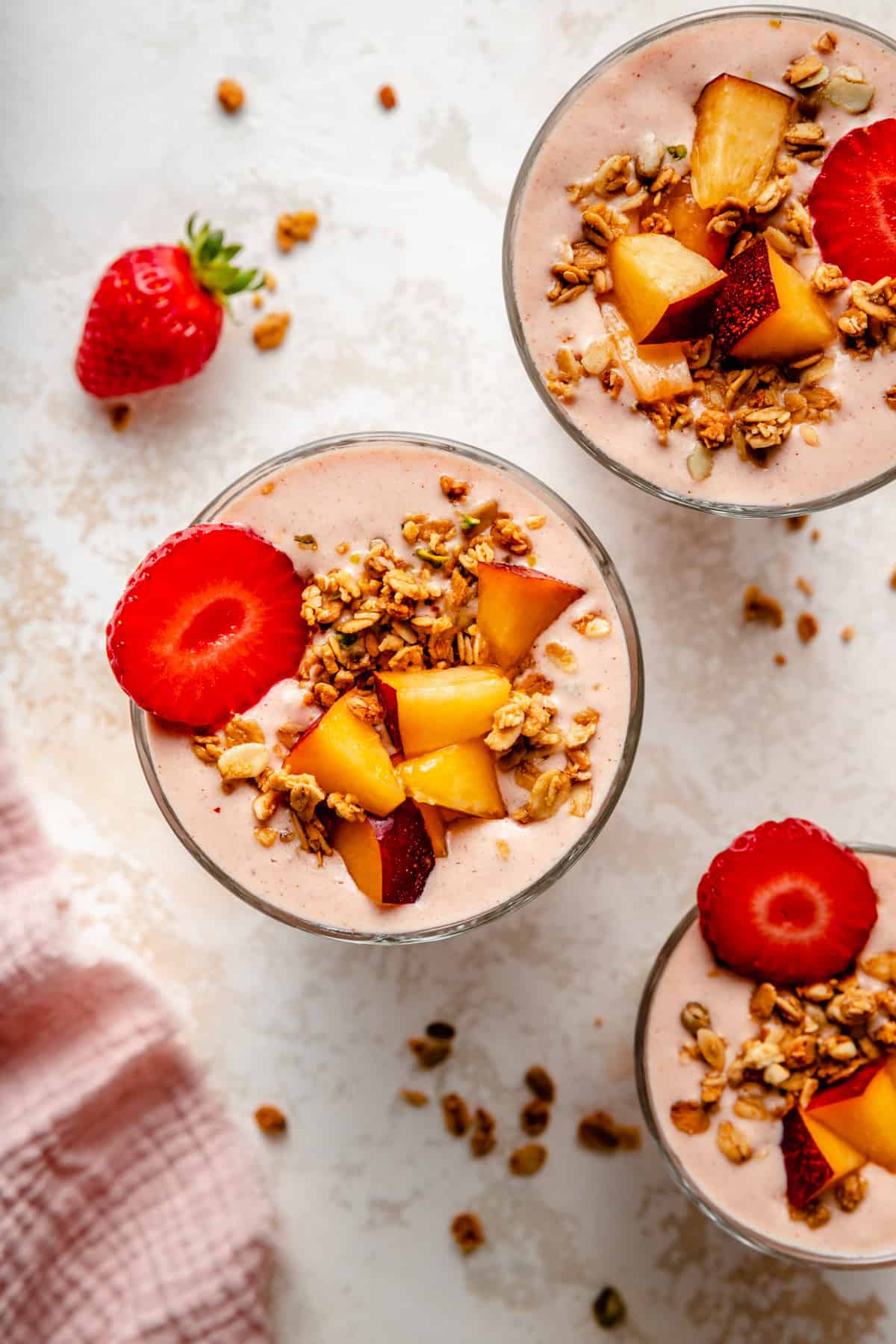 Multiple glasses of strawberry peach smoothie with fruit and granola toppings.