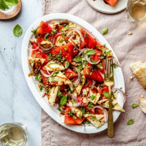 Watermelon basil salad served on a platter with balsamic glaze and a golden fork to the side.