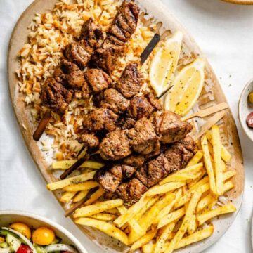 Lamb souvlaki served on a platter with rice, fries, tzatziki and greek salad.
