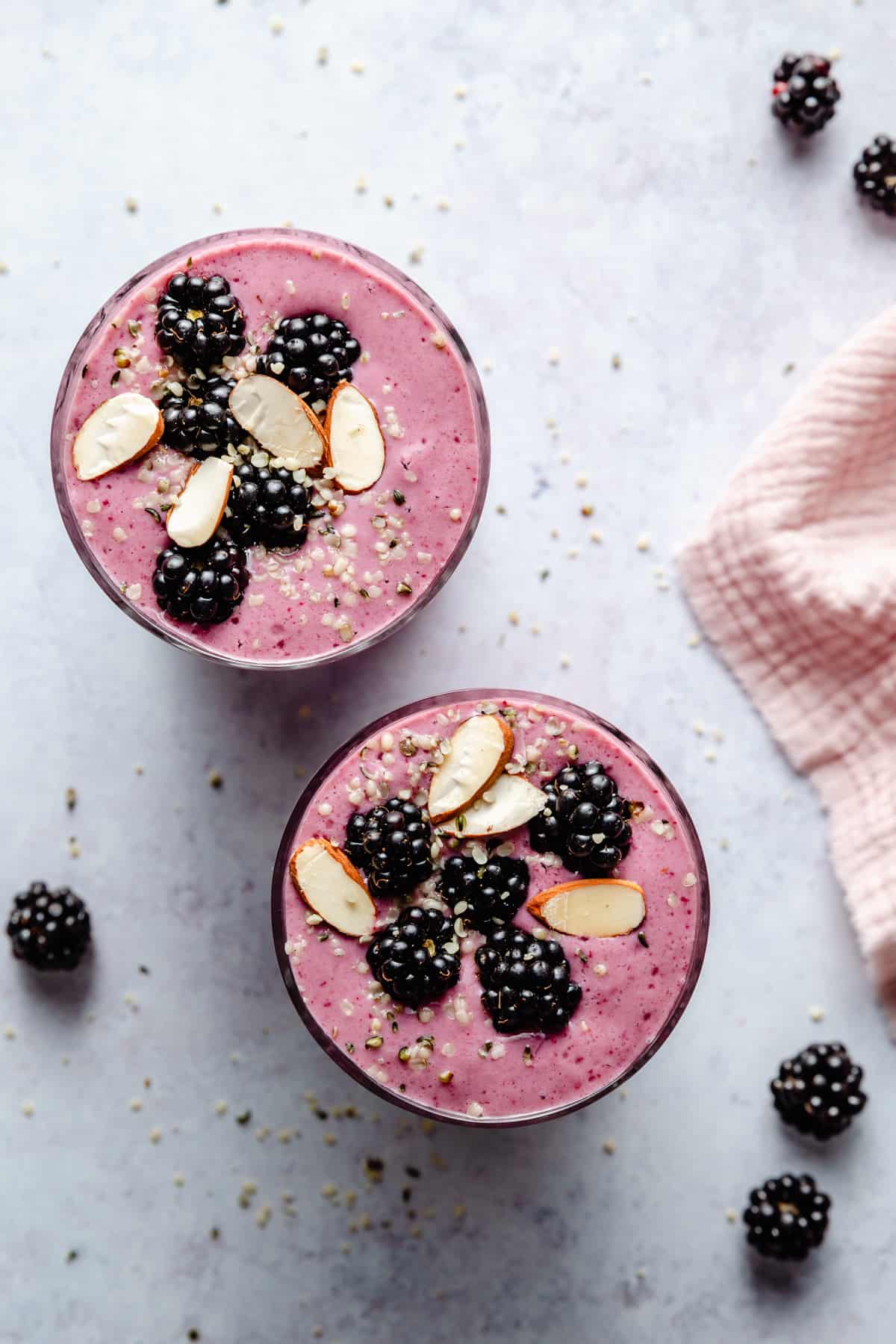 Overhead of two glasses of smoothie with blackberries and seeds on top with a napkin to the side.