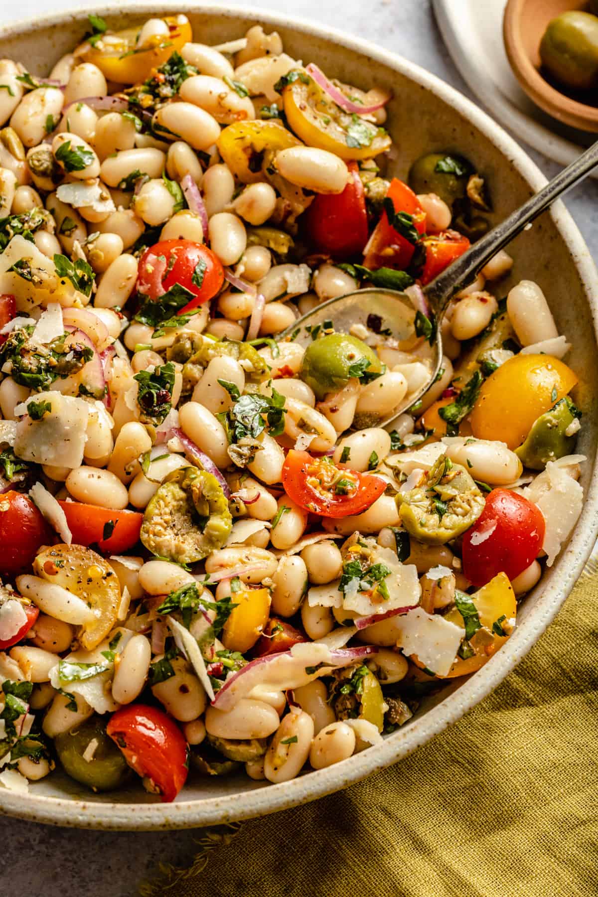 Close up of a bowl of a bean salad dressed in a herb salsa with a spoon and a napkin.