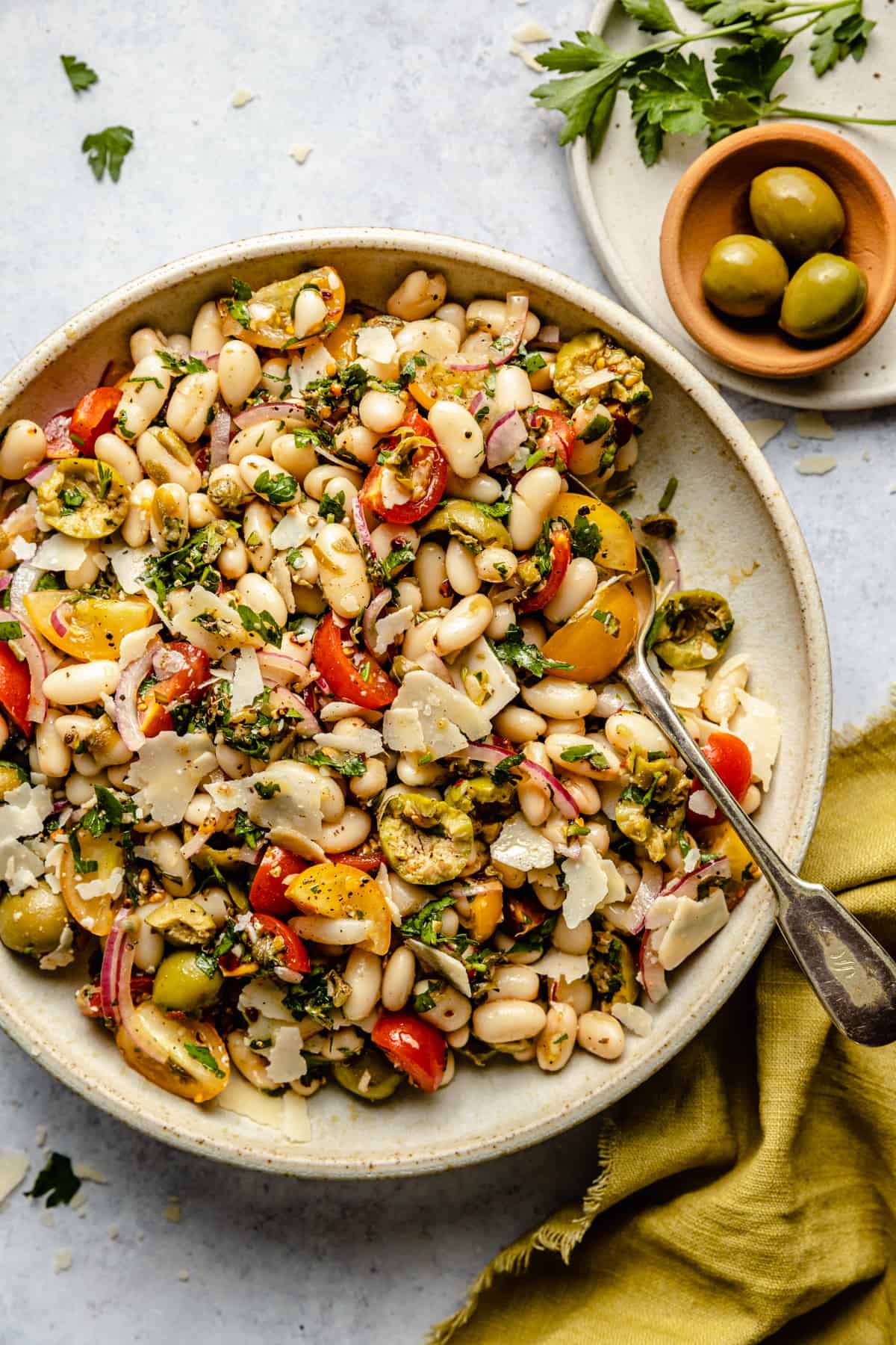 A bowl of white bean salad dressed in salsa verde being served with a spoon. 