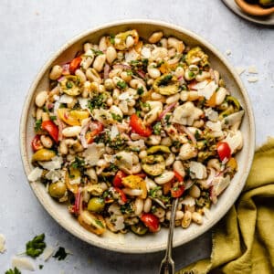 White bean salad dressed with salsa verde in a bowl with a spoon and a napkin to the side.