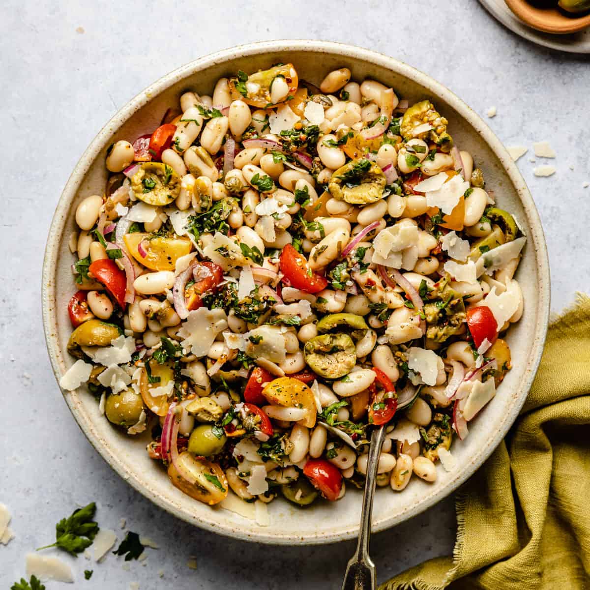 A bowl of white bean salad with a spoon and a napkin to the side. 