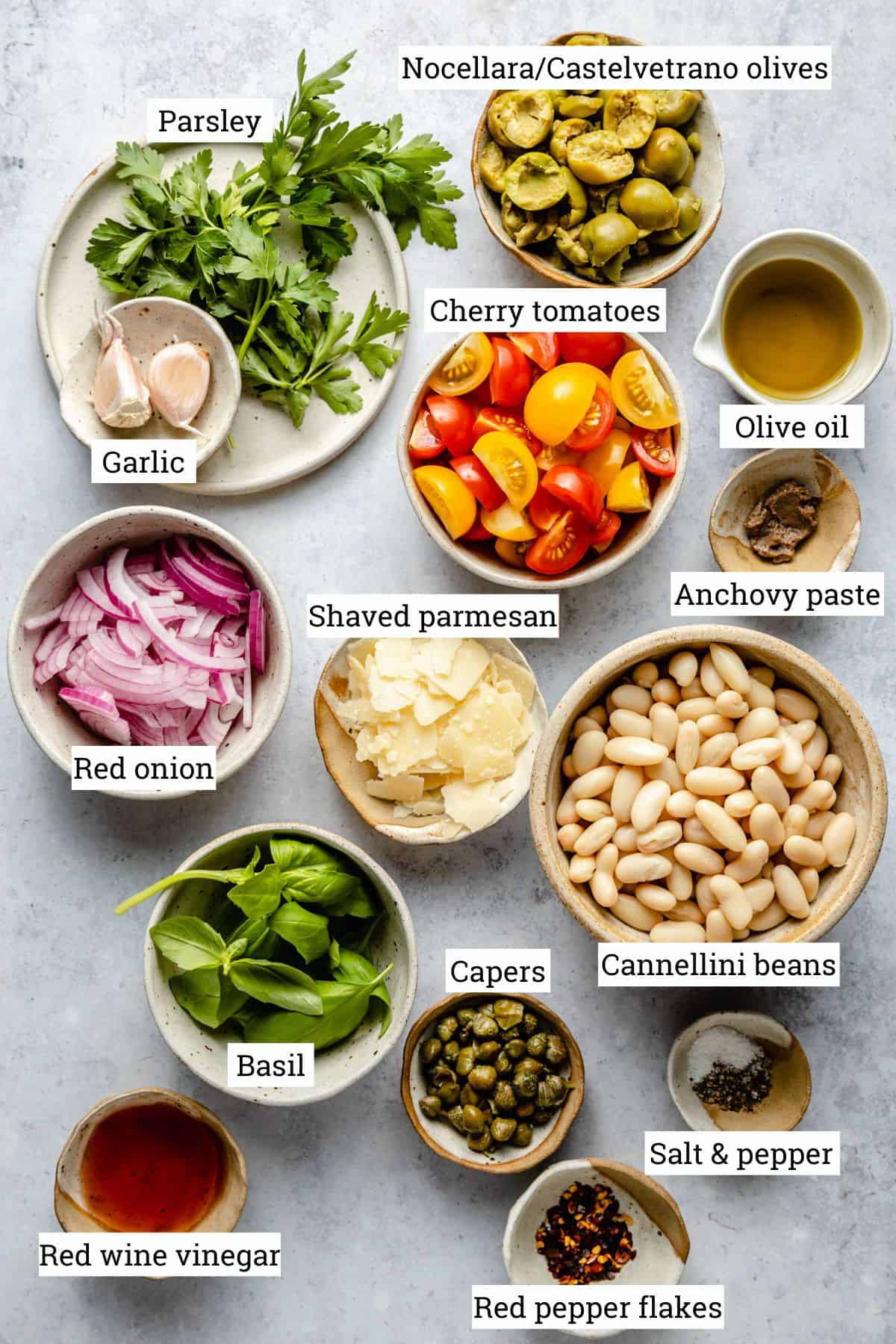 various bowls on a grey background containing the ingredients needed to make the salad.