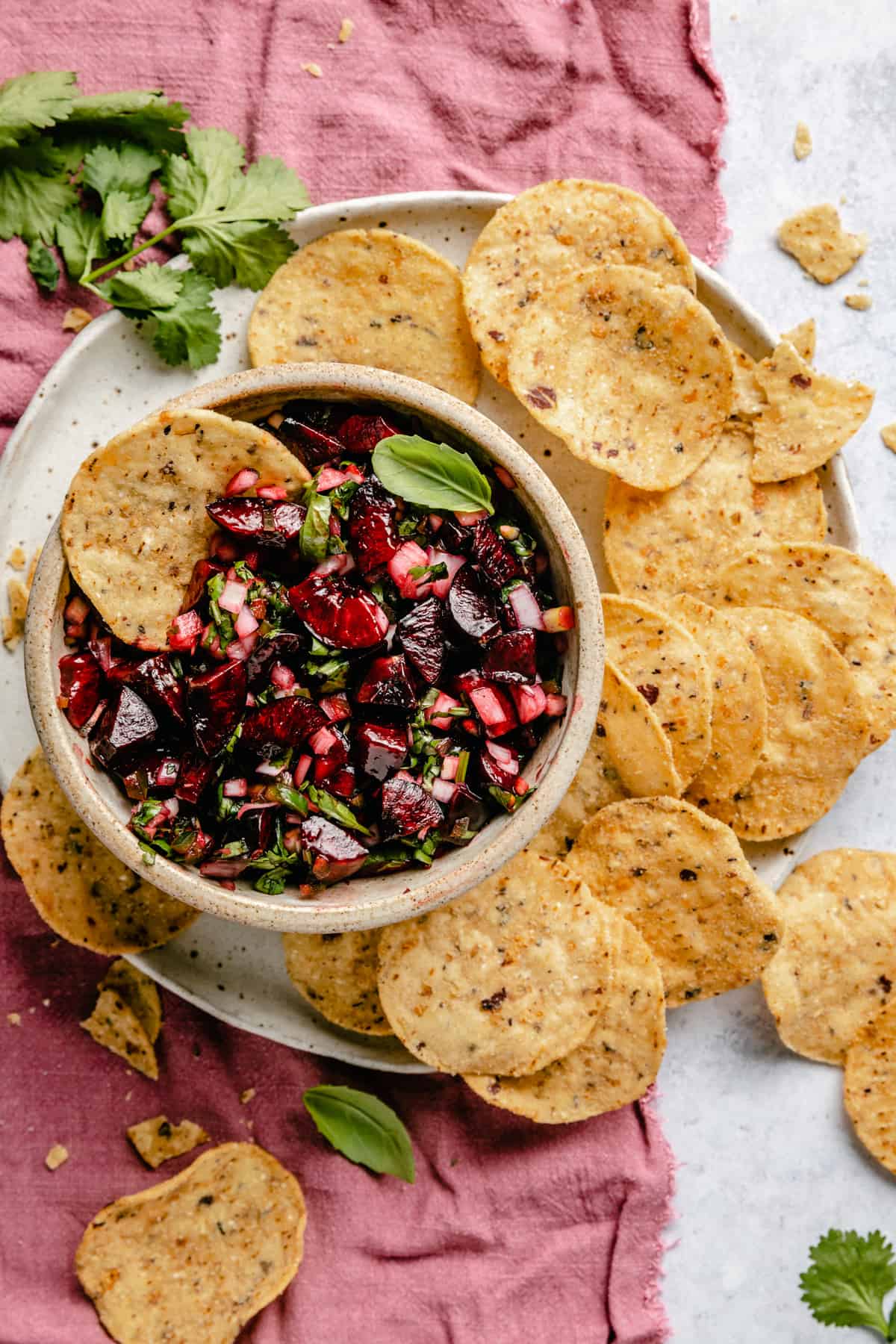 A bowl of cherry salsa with a chip dipping into it on a plate of chips with a napkin underneath.