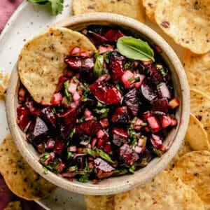 A bowl of cherry salsa on a plate with tortilla chips.