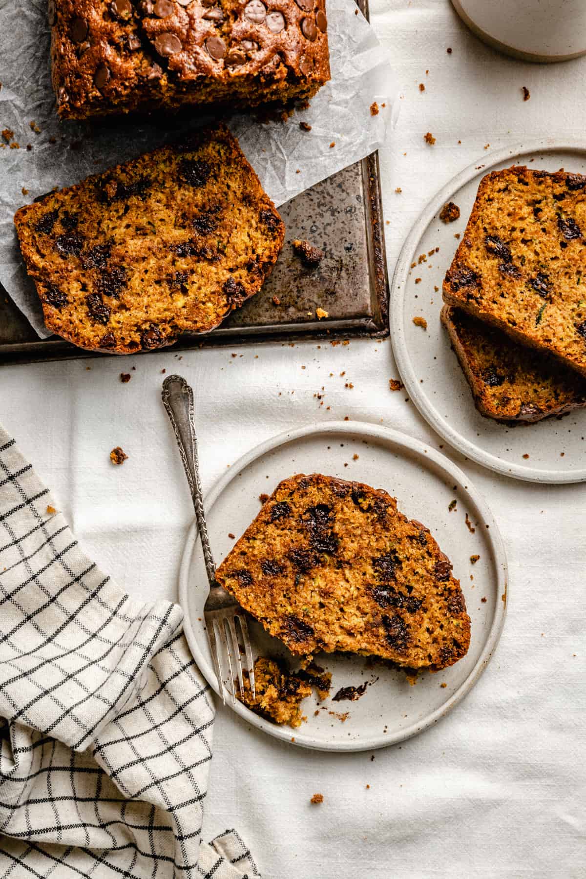 A couple of plates and a board with slices of chocolate chip zucchini bread with a fork and a chunk broken off.