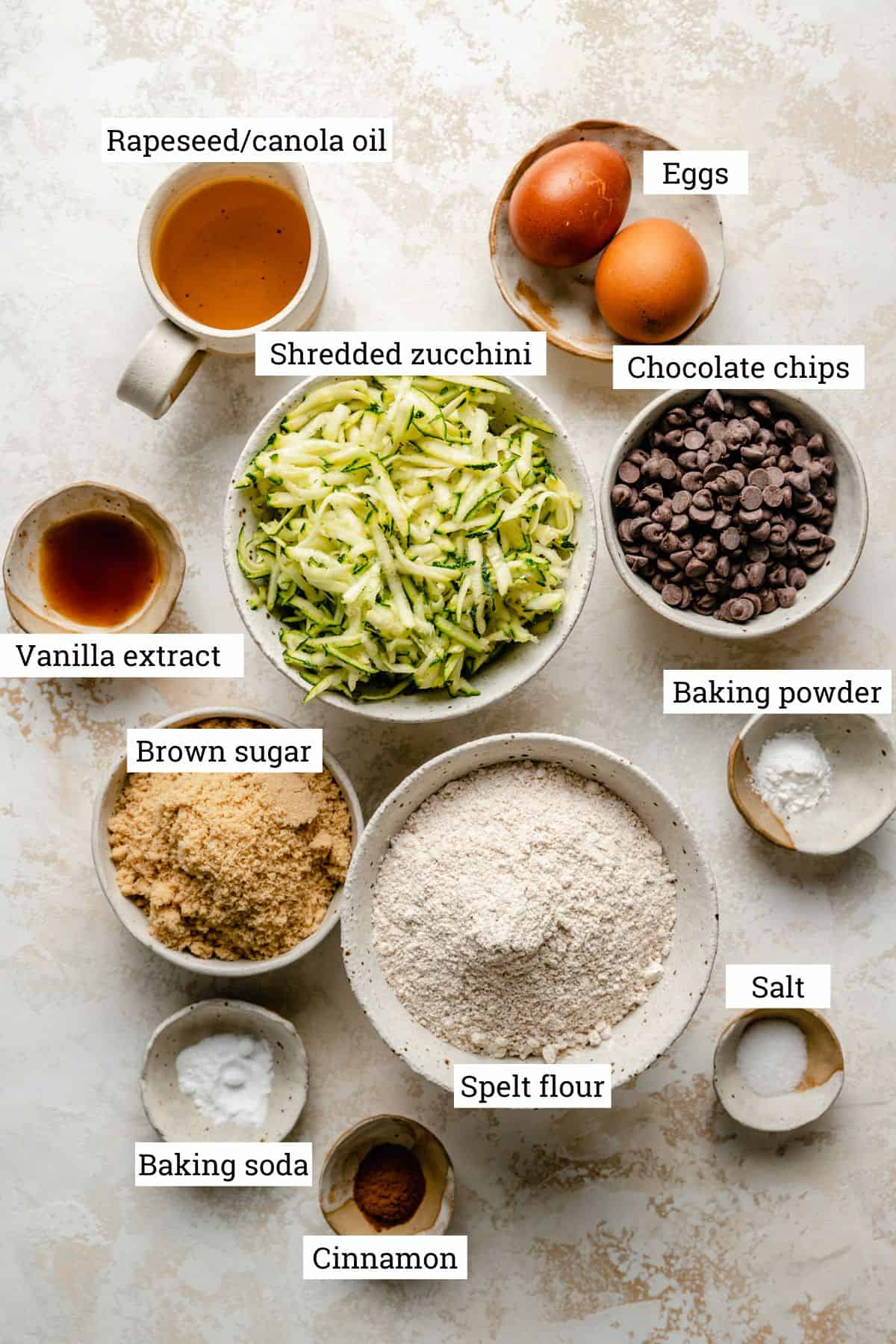 Ingredients in bowls including, grated zucchini, spelt flour, chocolate chips and eggs. 