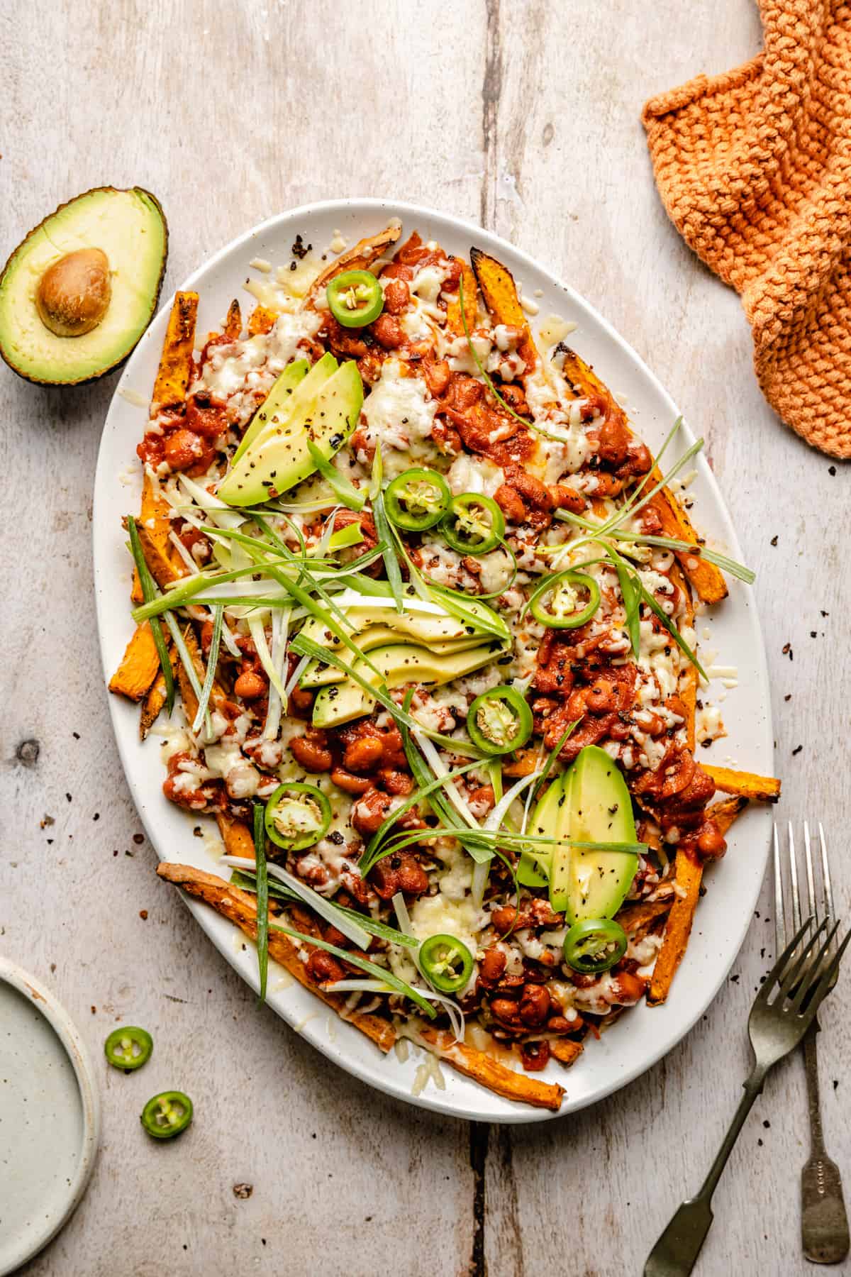 Loaded sweet potato fries on a platter with all the toppings a fork and napkin.