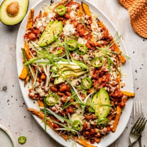 Loaded sweet potato fries on a platter with forks and napkin to the side.