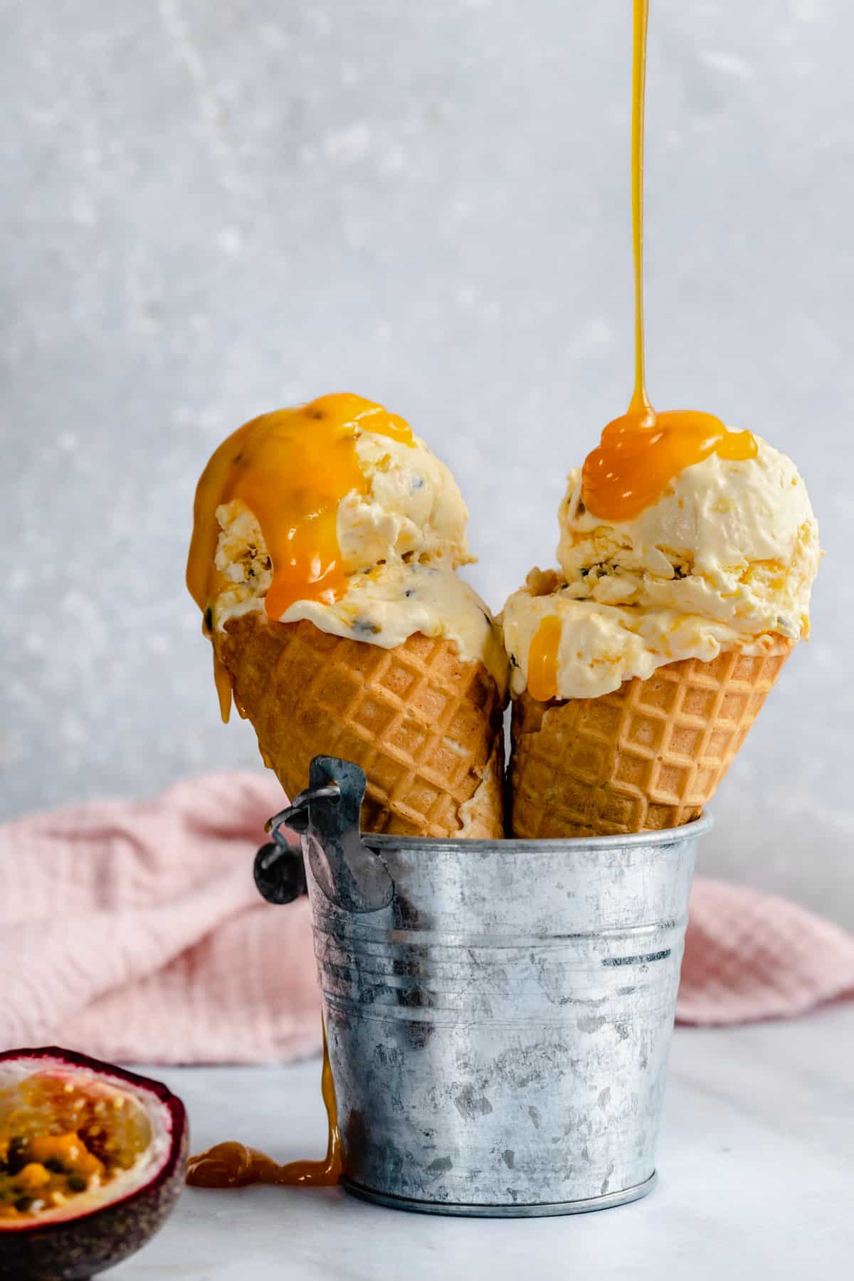 Two waffle cones with scoops of passion fruit ice cream with curd drizzled on the top.