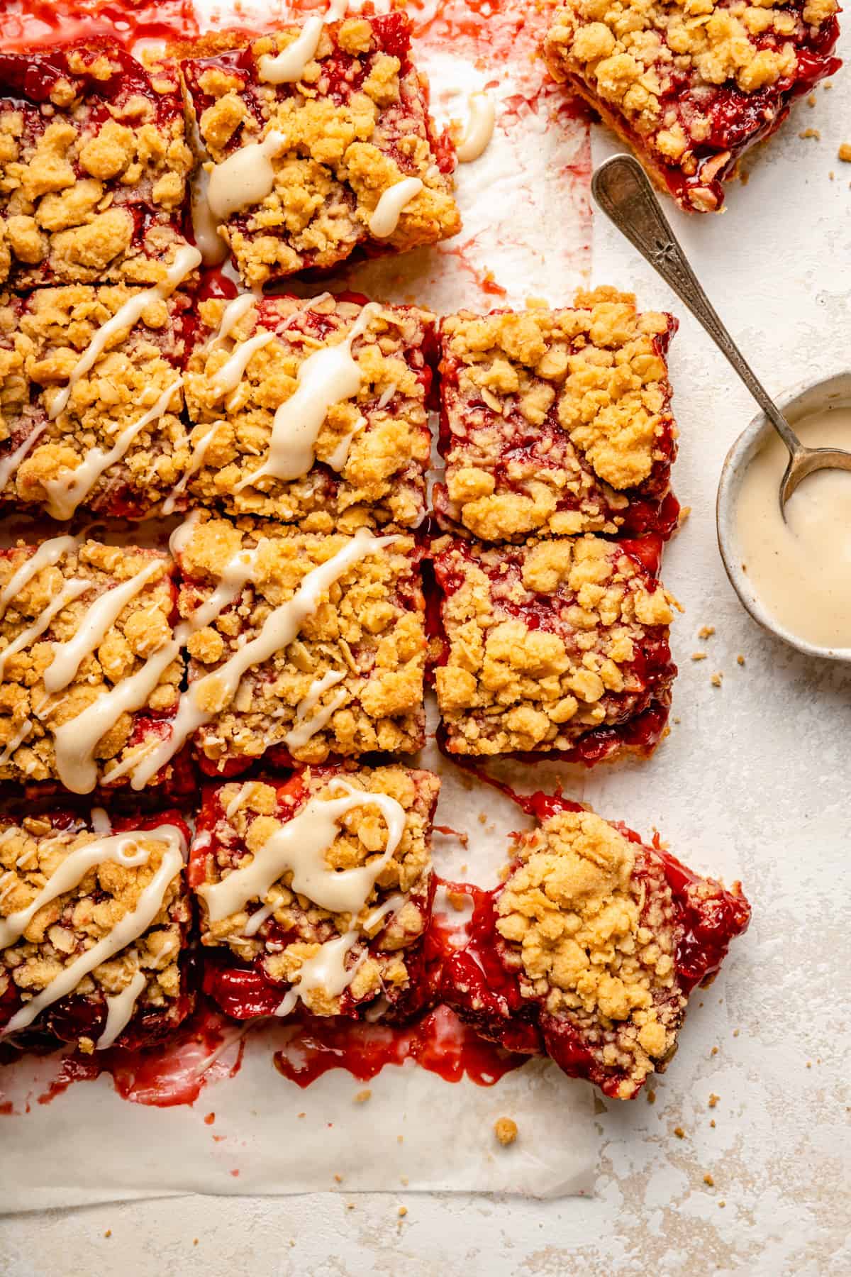 Overhead strawberry bars cut up on work surface, some topped with glaze and others pulled out.