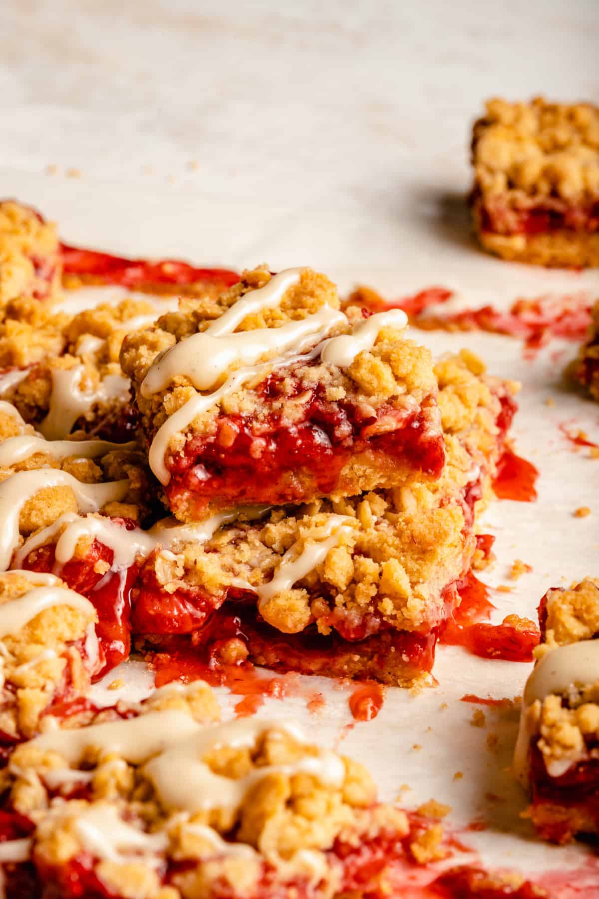 A stack of strawberry crumble bars on a work top with brown butter glaze drizzled over.