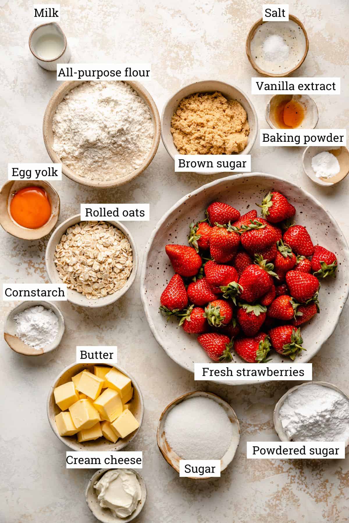 An array of bowls with ingredients including strawberries, flour, oats and sugars.