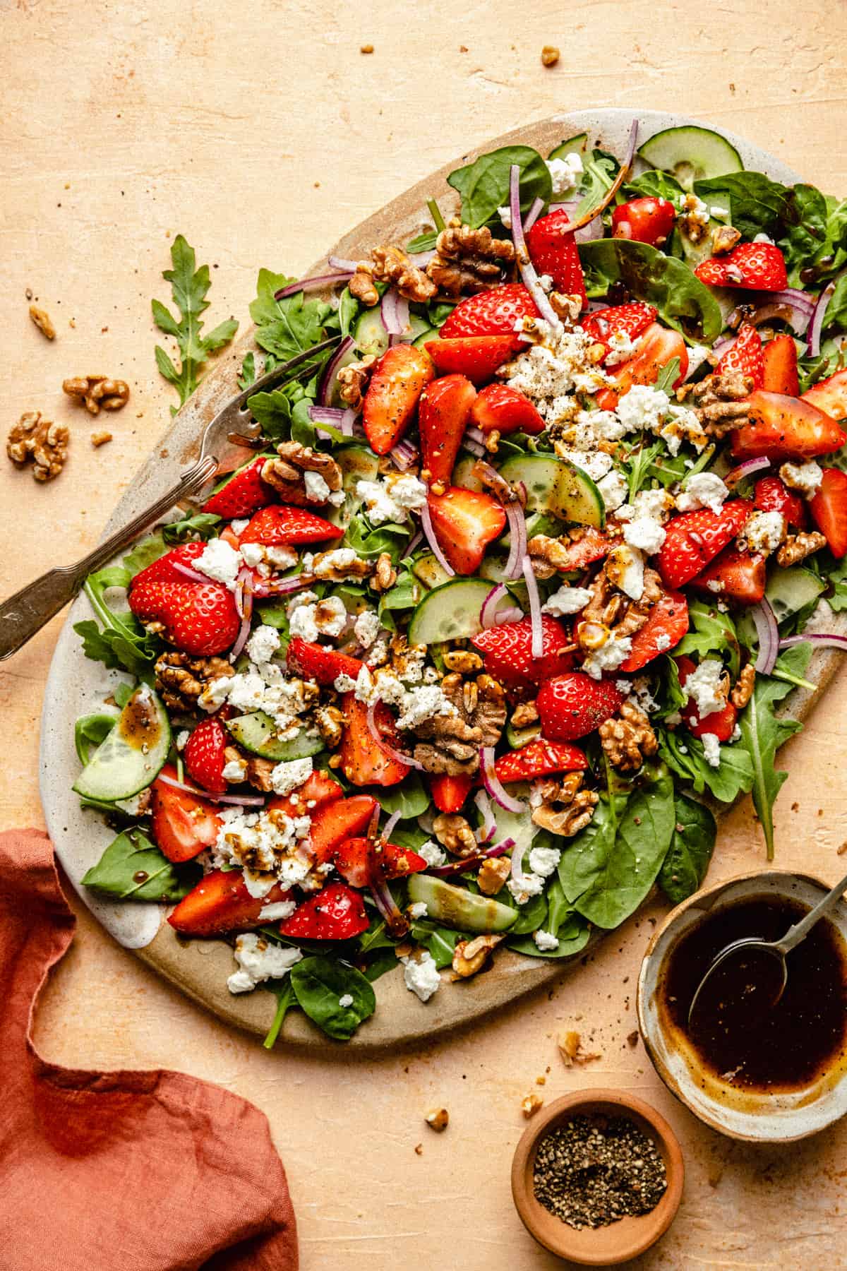 Strawberry walnut salad on a platter with a fork with walnuts and balsamic dressing to the side.