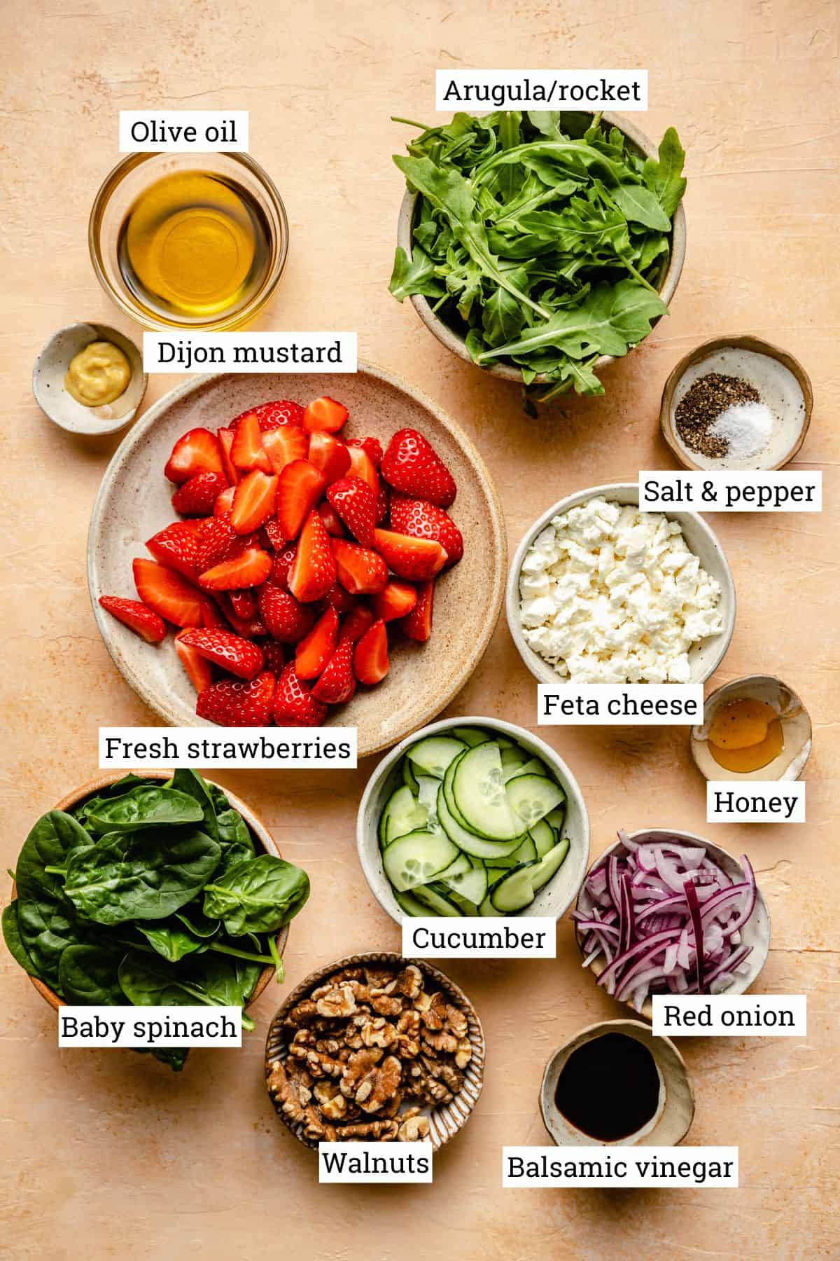 Bowls of ingredients with labels, including, strawberries, feta, spinach, walnuts and cucumber.