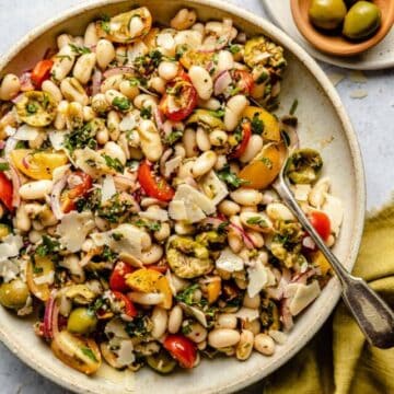 White bean salad dressed with salsa verde in a bowl with a spoon and napkin to the side with some olives.