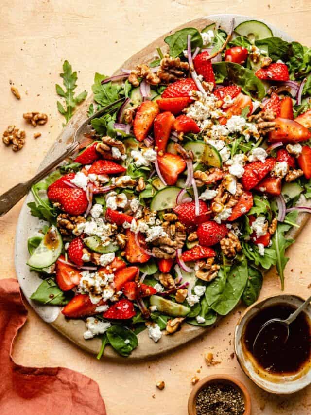 Strawberry walnut salad served on a platter with a fork and bowl of dressing to the side.