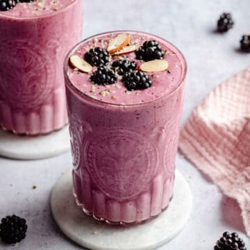 blackberry strawberry banana smoothie served in a glass on a marble coaster with fruit and nuts on top.