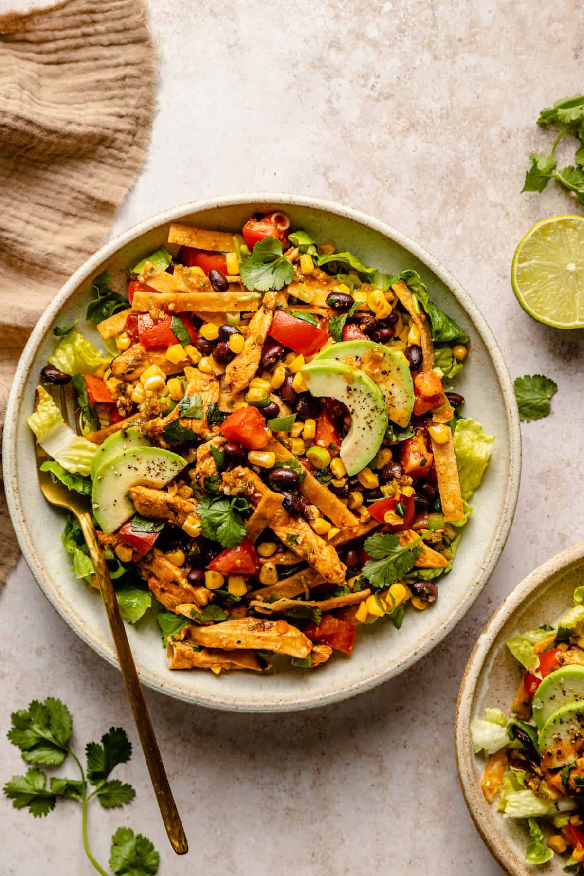 A large bowl with chicken tostada salad served inside with a fork, lime and napkin to the side.