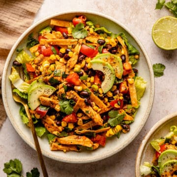 Chicken tostada salad served in a bowl with a fork with a lime and napkin to the side.