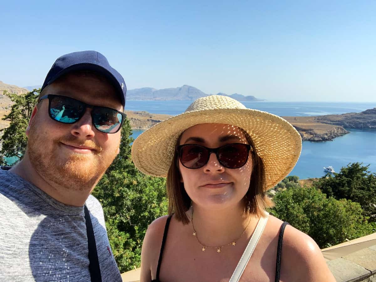 Jacob & Sasha wearing sunglasses and hats with a landscape view of Rhodes, Greece in the background.