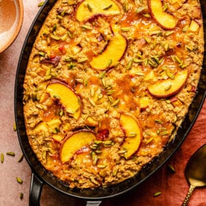 a close up of peach baked oatmeal in a baking dish with a spoon and bowl nearby.