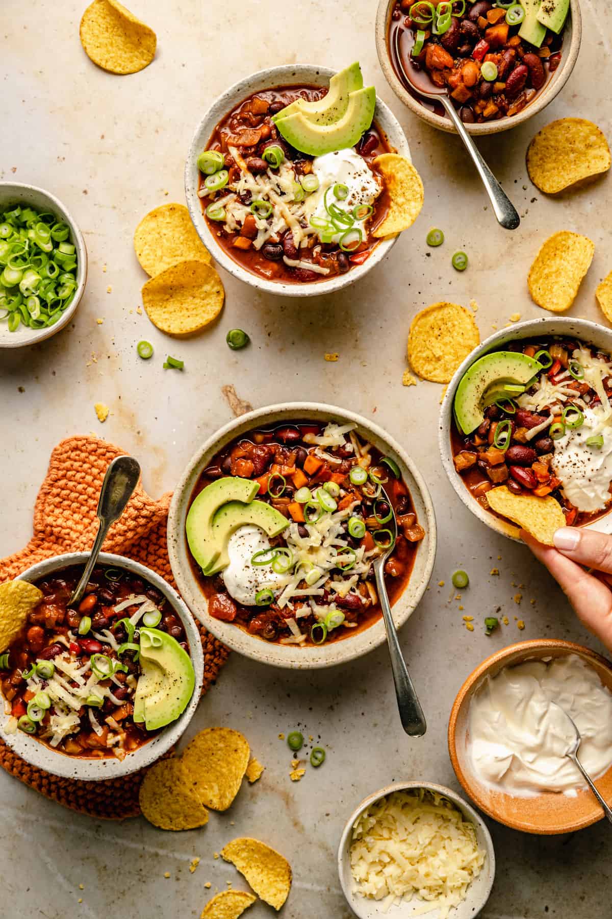 An array of 5 bowls of three bean chili, topped with cheese, sour cream avocado and onions.