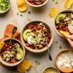 Three bean chilli served in various bowls with chips and toppings around.